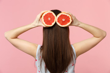Back rear view of young woman in summer clothes hold in hands halfs of fresh ripe grapefruit...