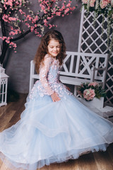Fototapeta premium Cute adorable baby girl in elegant blue wedding dress indoors posing and looking at camera. Childhood, fashion kids concept