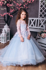 Fototapeta premium Cute adorable baby girl in elegant blue wedding dress indoors posing and looking at camera. Childhood, fashion kids concept