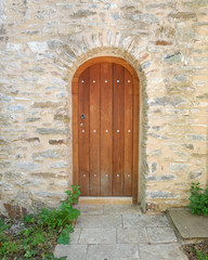 Fototapeta na wymiar arched wooden door on old stonewall, space for text