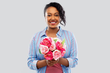 people and international women's day concept - happy african american young woman with bunch of peony flowers over grey background