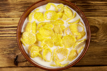 Cornflakes with milk in a bowl on wooden table. Top view