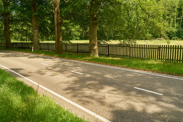 Obraz premium Gerade Landstraße vor Zaun mit Wiese