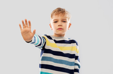 restriction, prohibition and children concept - little boy in striped pullover making stopping gesture over grey background