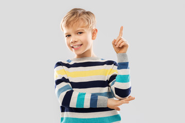 childhood, expressions and people concept - little boy in striped pullover pointing finger up over grey background