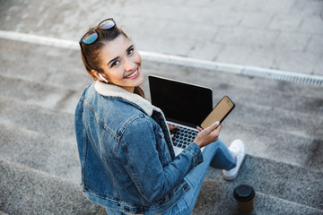 Fototapeta premium Smiling young woman wearing jacket sitting on a bench