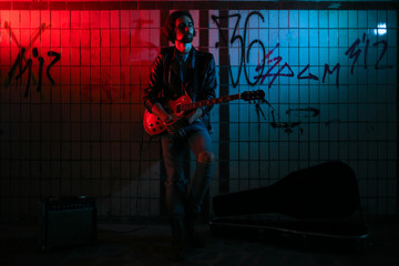 Fototapeta na wymiar A street musician playing on guitar in the underpass. Vagrant lifestyle. Playing in the underpass to make a living. Unemployed musician. Future rock star.