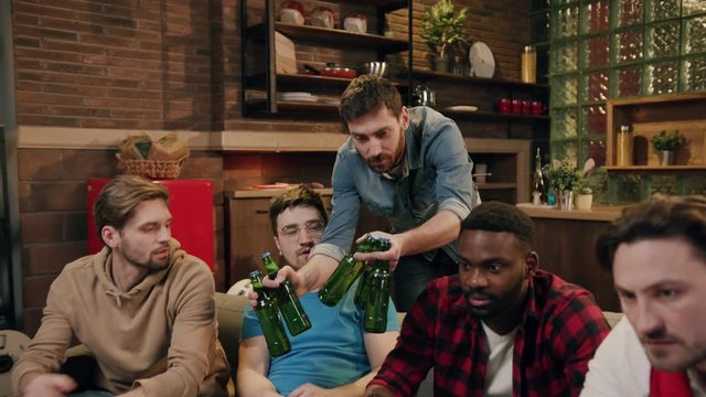 Four cheerful male football fans cheering for their teams at home by the TV with football attributes. Standoff, true friendship, entertainment concept. Home party, drinking beer, eating snacks by tv