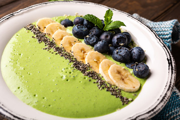 Breakfast detox green smoothie bowl from banana and spinach on wooden background. Healthy food concept