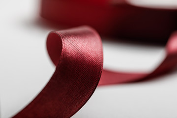 selective focus of shiny silk curved burgundy ribbon on grey background