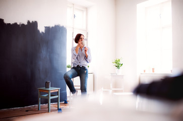 A portrait of young woman painting wall black. A startup of small business.