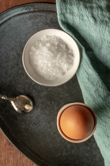 A photo of a boiled egg with coarse sea salt, shot from the top on a dark rustic wooden background with a place for text