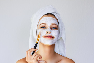 Beautiful young woman applying facial mask on her face with brush. Skin care and treatment, spa,...