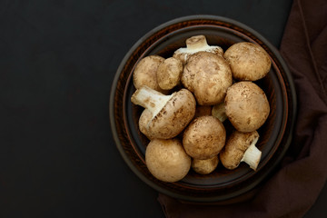 Brown champinon mushrooms (agaricus) in bowl on rustic wooden background. Healthy eating or vegetarian concept. Copy space. Top view