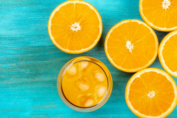 A photo of a glass of fresh orange juice with orange halves, shot from above on a vibrant blue background with a place for text