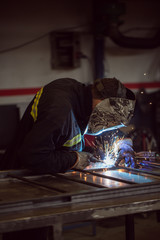 Worker grinding on a metal gate, at his workshop, wearing safety helmet