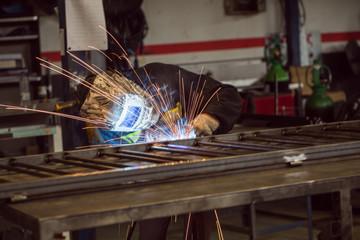 Worker grinding on a metal gate, at his workshop, wearing safety helmet