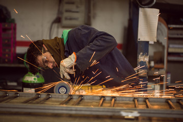 Worker grinding on a metal gate, at his workshop, wearing safety glasses