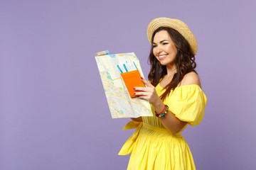 Smiling young woman in yellow dress, summer hat hold city map, passport boarding pass ticket isolated on pastel violet wall background. People sincere emotions, lifestyle concept. Mock up copy space.