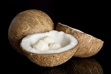 Group of one whole two halves of fresh bio coconut with three small cocoa balls isolated on black glass