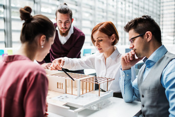 Group of young architects with model of a house working in office, talking.
