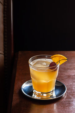 Amaretto Sour Cocktail on the Rocks with a Cherry and Orange Garnish in a Dark Luxurious Bar