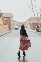 Fashionable young woman wetting her skirt and smiling in the rain with black boots and printed long skirt