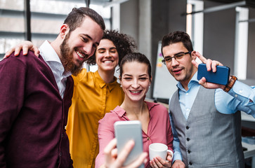 A group of young businesspeople with smartphone in office, taking selfie.