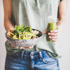 Healthy dinner or lunch. Woman in t-shirt and jeans standing and holding vegan superbowl or Buddha bowl with hummus, vegetable, salad, beans, couscous and avocado and smoothie in hands, square crop - obrazy, fototapety, plakaty