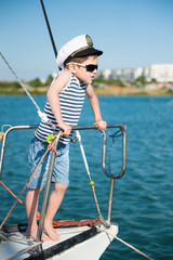 Obraz premium cute little caucasian boy in sunglasses and captain cap on white yacht board