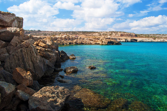 Image of Blue Lagoon bay near Cape Greco, Cyprus. View of rock coastline near deep green transparent emerald water against a rocky hill. Amazing cloudscape. Warm day in fall