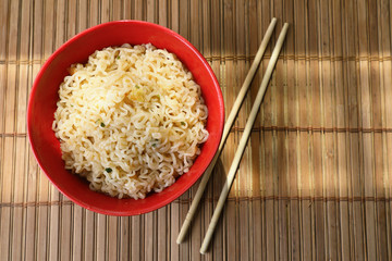  Asian style noodles in a red Cup with chopsticks. against a bamboo Mat .  the view from the top .