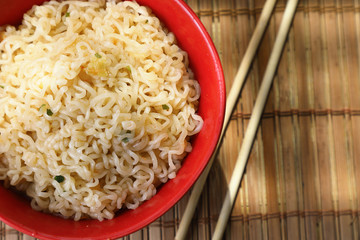 Asian style noodles in a red Cup with chopsticks. against a bamboo Mat .