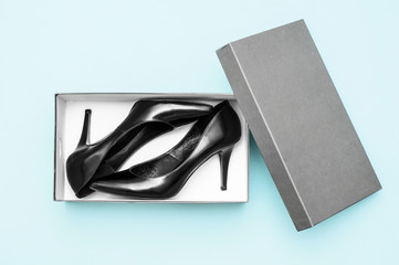 Black classic high heel shoes in gray box. Sky blue background. Stylish lady. Flat lay. Top view
