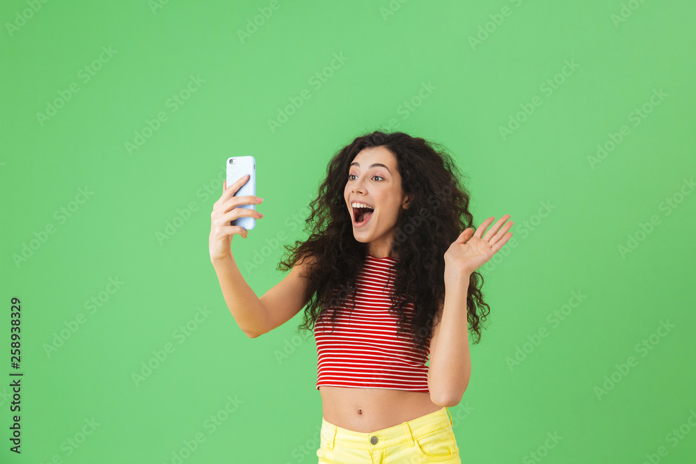 Poster photo of brunette woman smiling and using cell phone isolated over green background