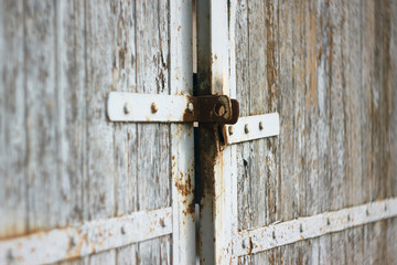 Old wooden gate with rusty latch and painted white. White paint flakes with time.