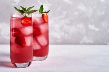 Fresh strawberry lemonade with ice and mint in glass on gray table background, copy space. Cold summer drink. Sparkling glasses with berry cocktail - obrazy, fototapety, plakaty