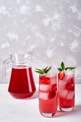 Fresh strawberry lemonade with ice and mint in glass on white table background, copy space. Cold summer drink. Sparkling glasses with berry cocktail