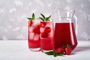 Fresh strawberry lemonade with ice and mint in glasses and jug on white table background, copy space. Cold summer drink. Sparkling glass with berry cocktail