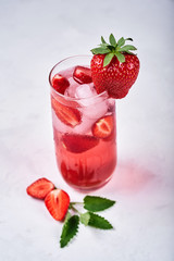 Fresh lemonade with ice, mint and strawberry on top in glass on white table background, copy space. Cold summer drink. Sparkling glasses with berry cocktail