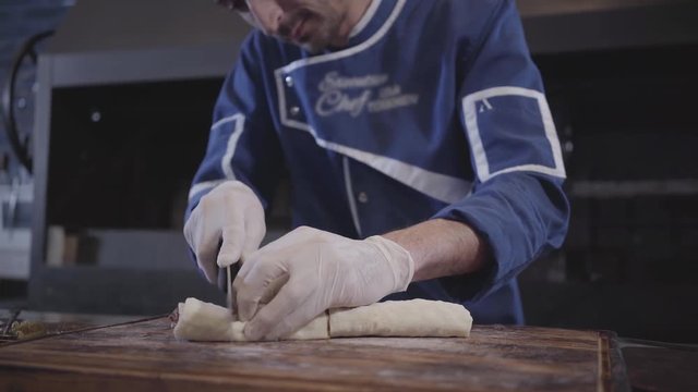 Skillful man in blue chef uniform cooking lula kebab in modern turkish restaurant. Cook cuts kebab wrapped in pita lavash with big sharp knife in pieces close up