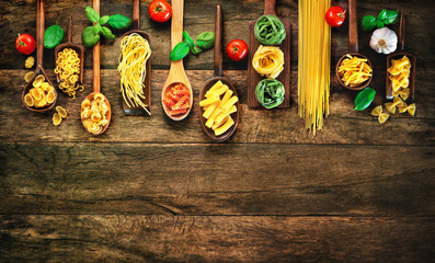 Various pasta on wooden spoons on wooden background