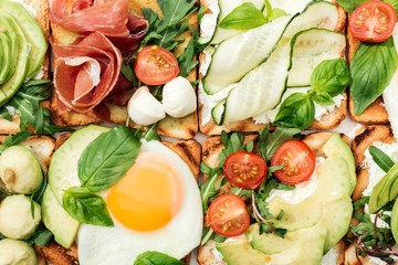 Top view of toasts with cut vegetables and prosciutto