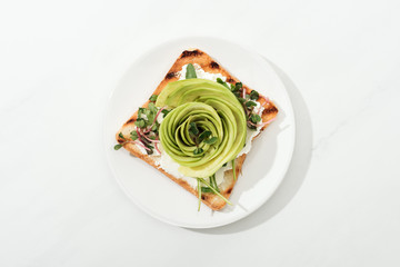 Top view of toast with sliced avocado and garden cress on plate on white surface