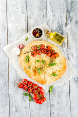 Traditional  homemade Italian flat bread focaccia. Focaccia with tomatoes and basil leaves, wooden background, top view