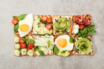 Top view of toasts with vegetables, fried eggs and prosciutto on textured surface