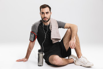 Handsome young sports fitness man posing isolate over white wall background listening music with earphones.