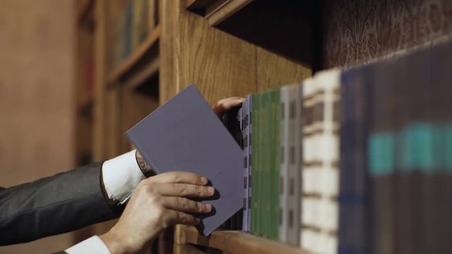 Male right hand choosing and picking book in public library. Pulling off selected textbook. Education research and self learning in university life concepts. Education and library concept.