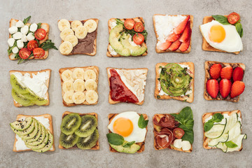 Top view of toasts with fried eggs, cut vegetables and fruits on textured surface