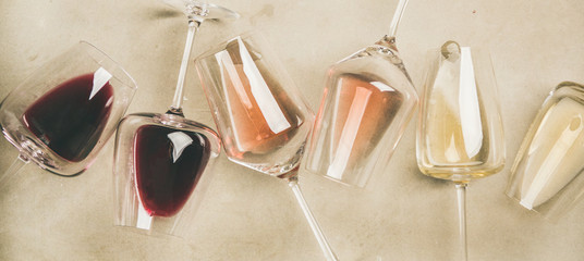 Flat-lay of red, rose and white wine in glasses over grey concrete background, top view, wide...
